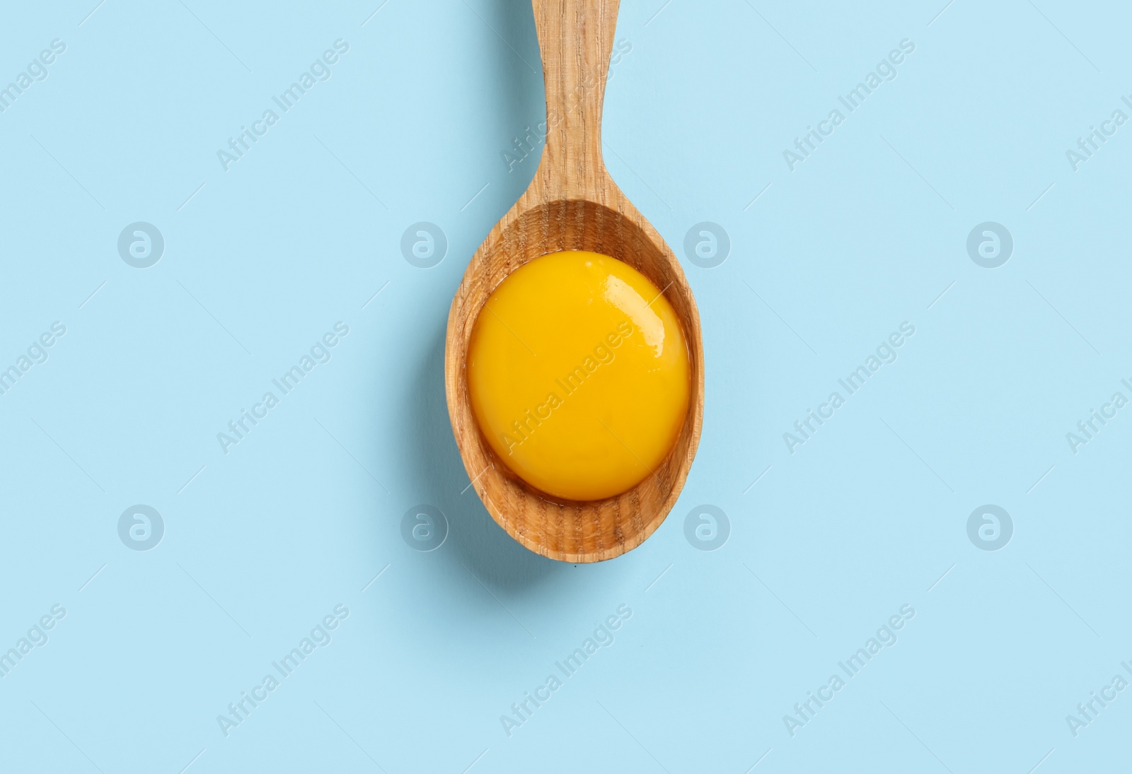 Photo of Wooden spoon with raw egg yolk on light blue background, top view