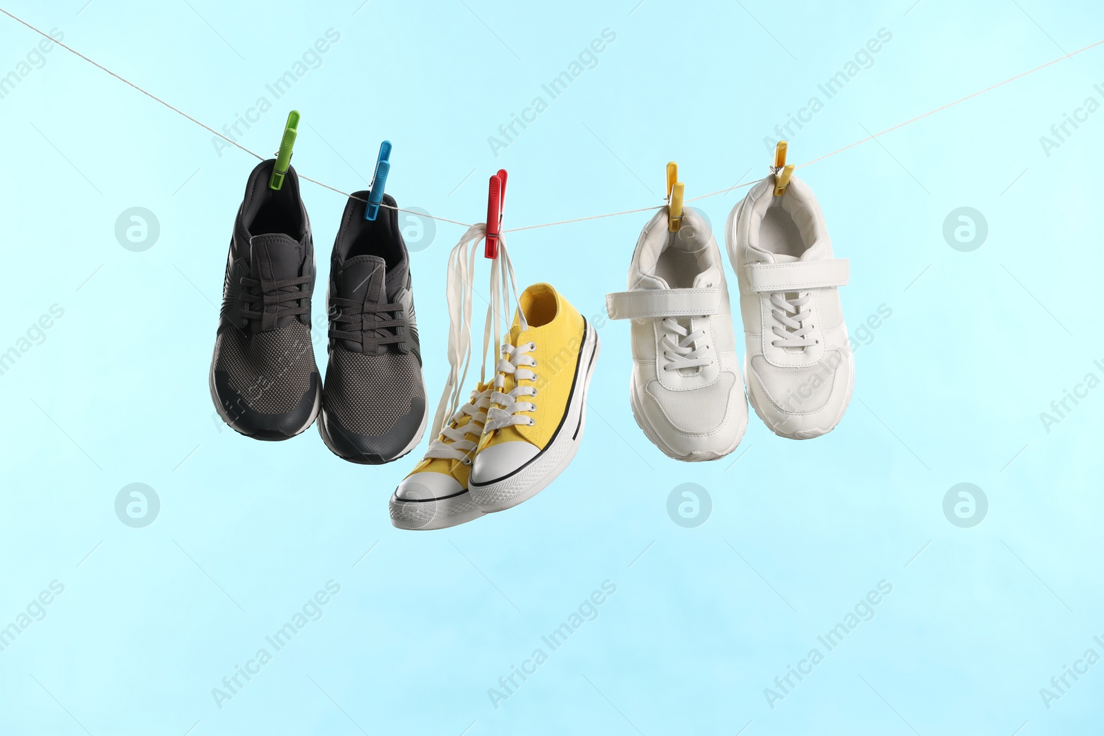 Photo of Different stylish sneakers drying on washing line against light blue background