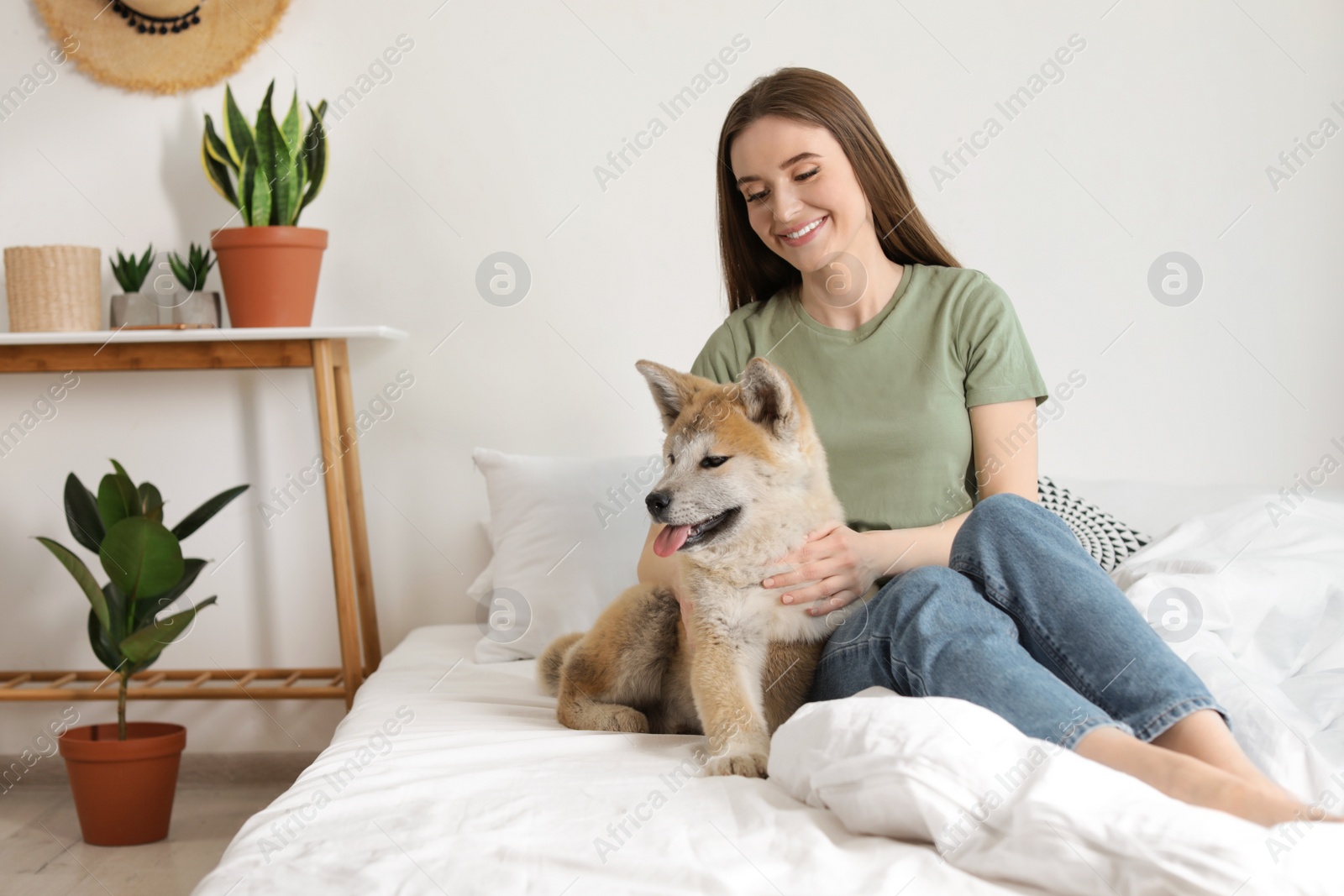 Photo of Young woman and Akita Inu dog in bedroom decorated with houseplants