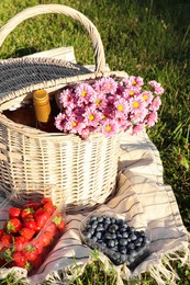 Picnic basket with flowers, bottle of wine and berries on blanket outdoors