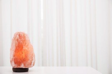 Photo of Himalayan salt lamp on white table indoors. Space for text