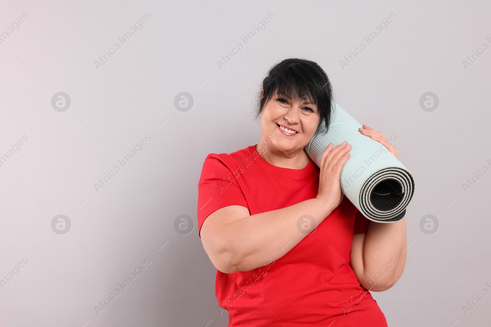 Photo of Happy overweight mature woman with yoga mat on grey background, space for text