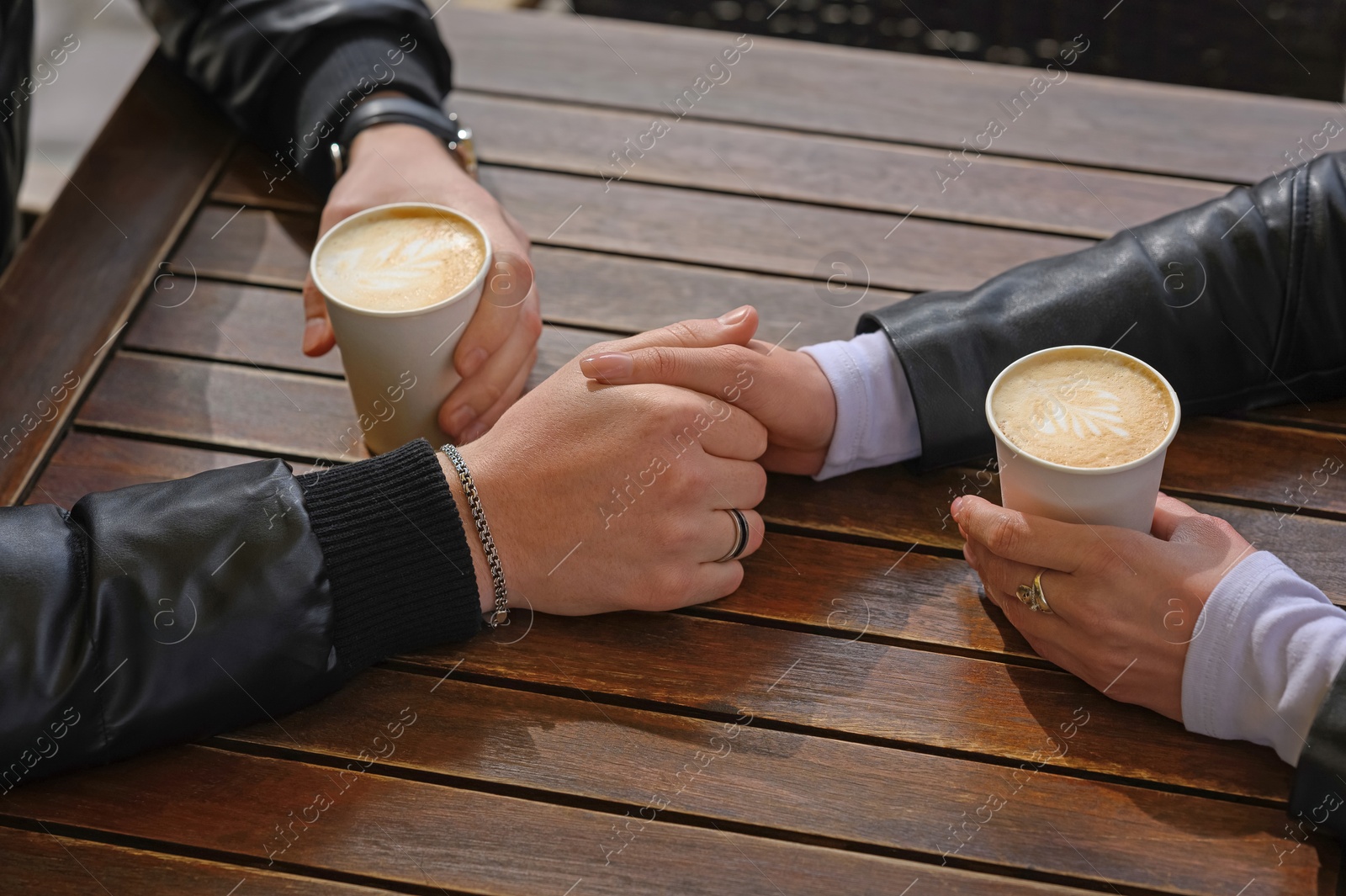 Photo of Lovely couple with coffee holding hands together at wooden table, closeup. Romantic date