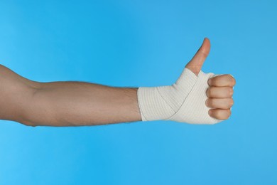 Photo of Man with hand wrapped in medical bandage showing thumbs up on light blue background, closeup