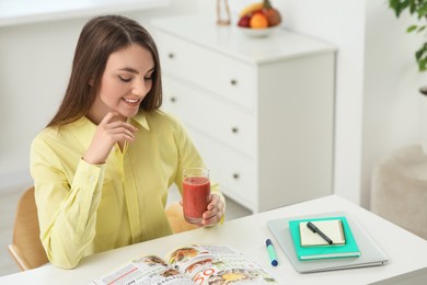 Beautiful young woman with delicious smoothie at table indoors