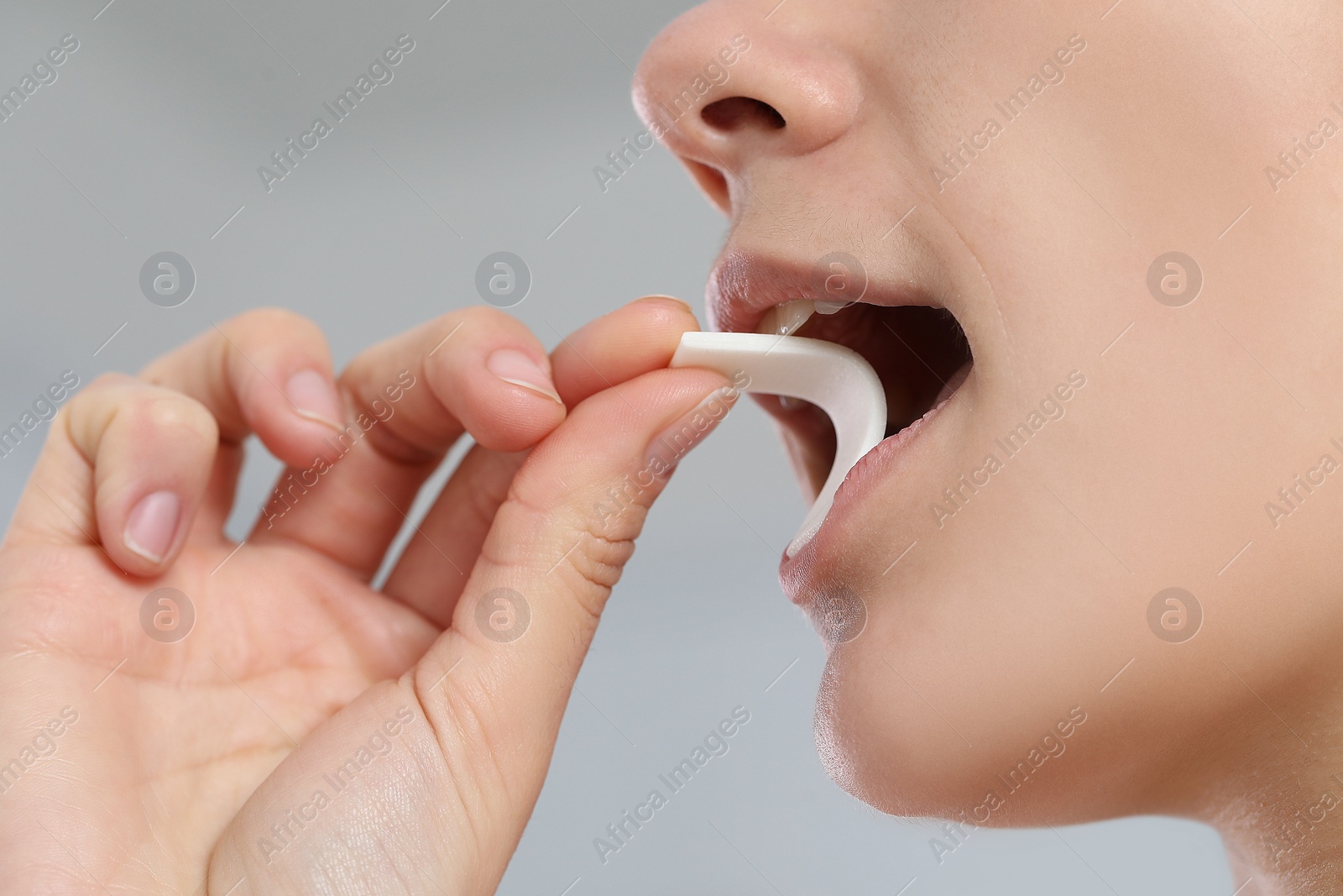 Photo of Woman putting chewing gum into mouth on blurred background, closeup