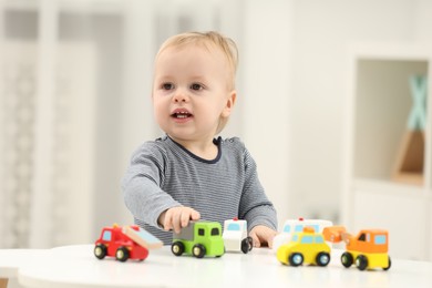 Children toys. Cute little boy playing with toy cars at white table in room