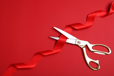 Photo of Stylish scissors and red ribbon on color background, flat lay with space for text. Ceremonial tape cutting