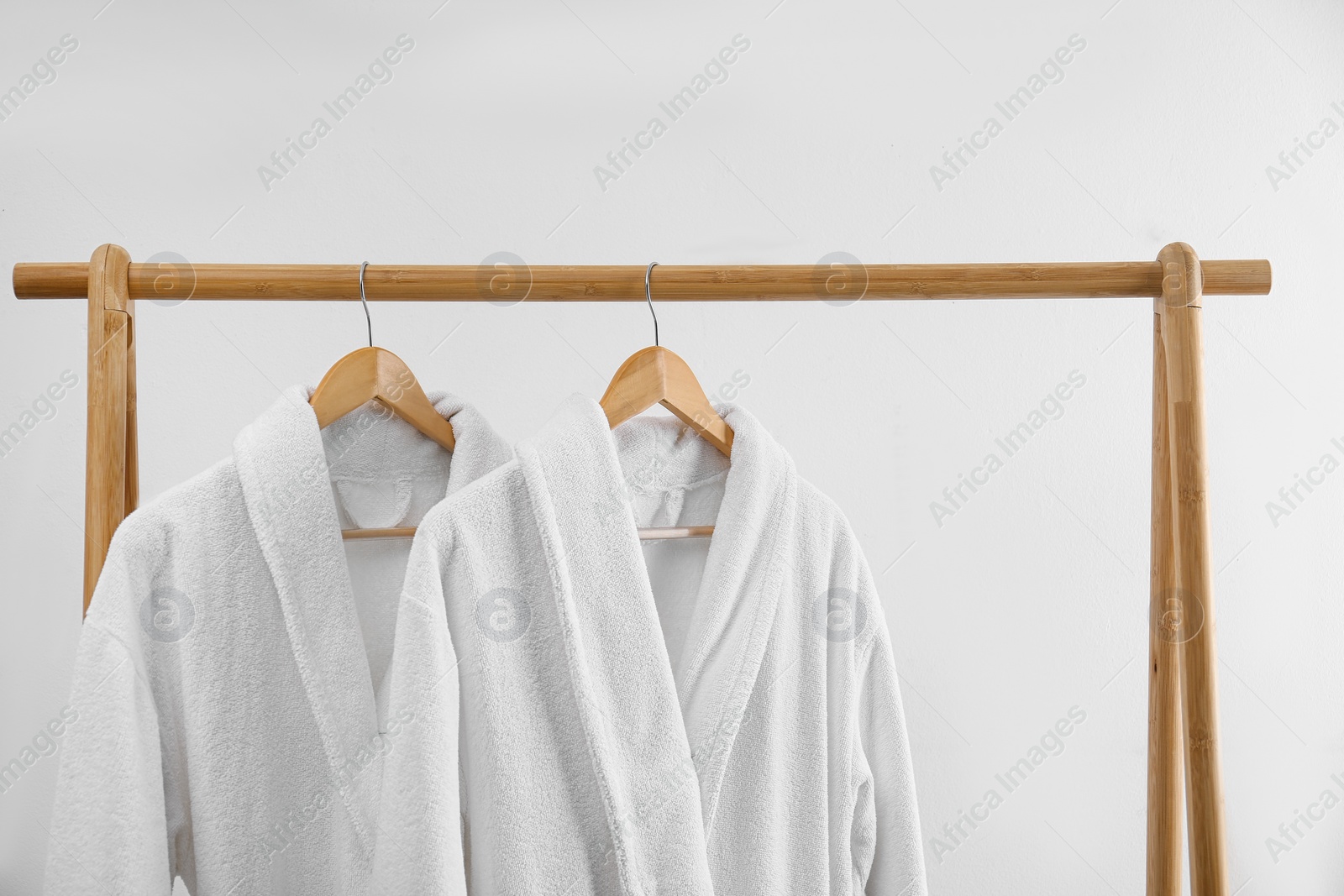 Photo of Fresh bathrobes hanging on rack near white wall