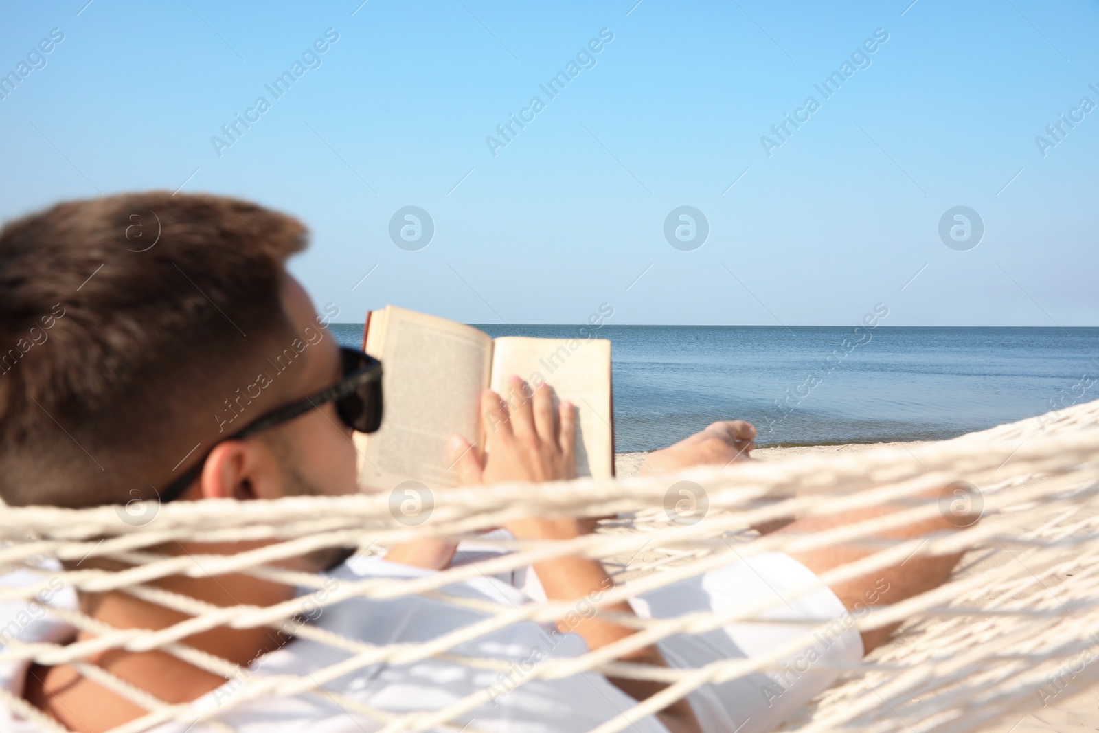 Photo of Young man reading book in hammock on beach