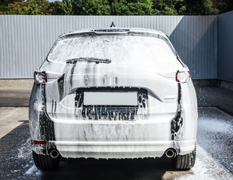 Luxury automobile covered with foam at car wash, back view