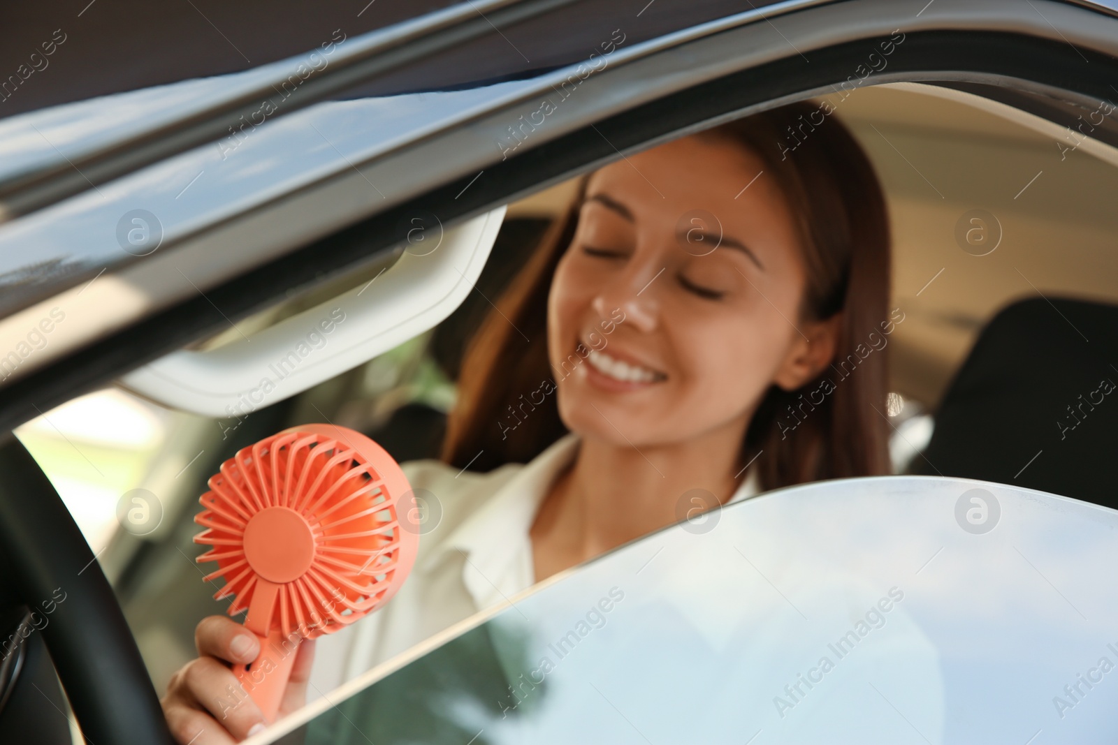 Photo of Young woman enjoying air flow from portable fan in car on hot summer day