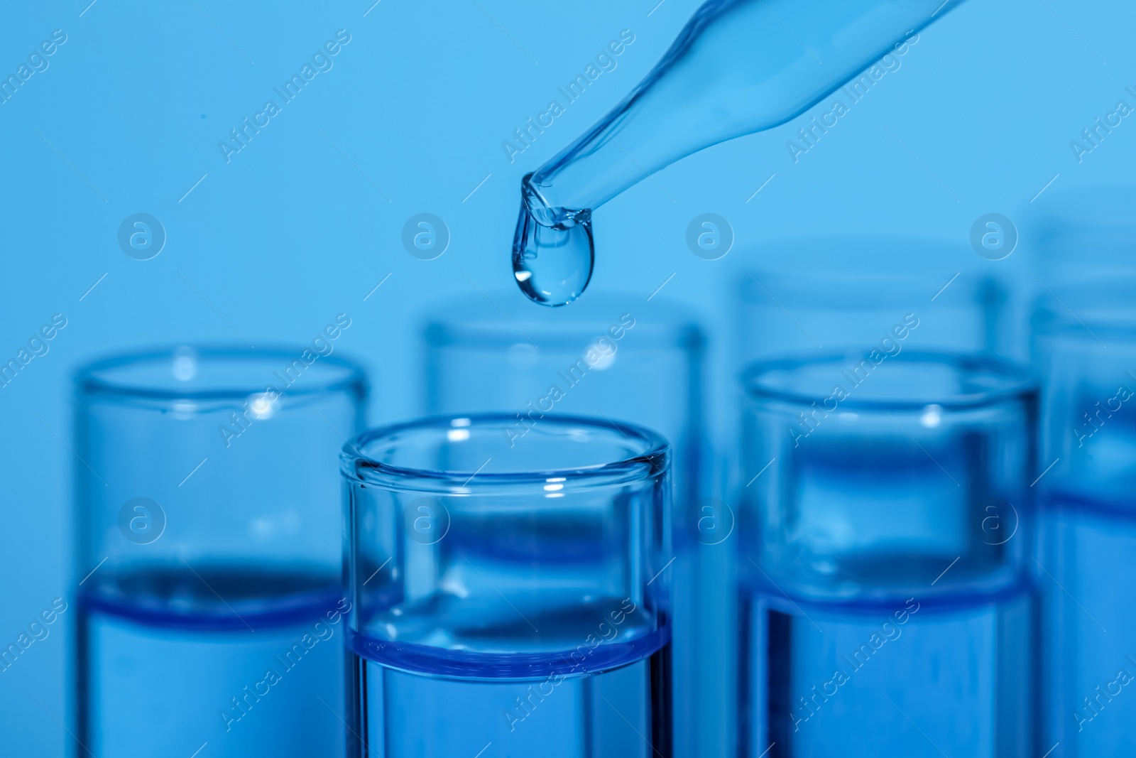 Photo of Dripping reagent into test tube on light blue background, closeup. Laboratory analysis