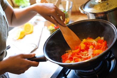 Photo of Woman cooking vegetables in frying pan indoors, closeup