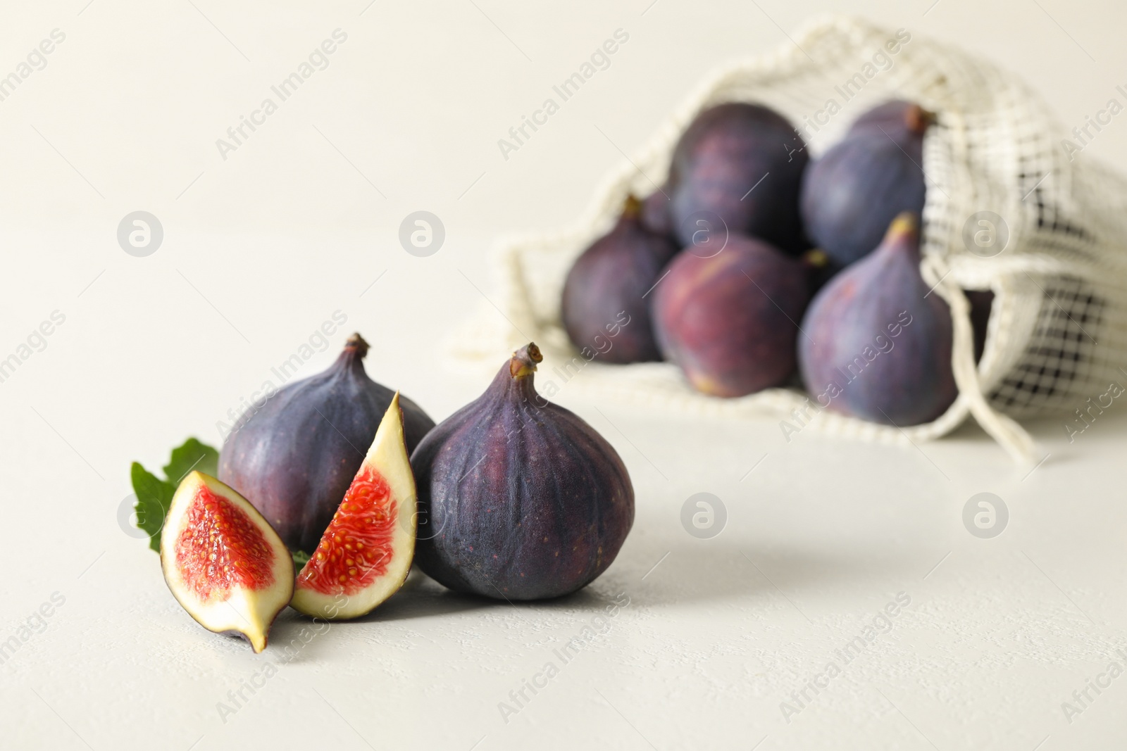 Photo of Whole and cut tasty fresh figs with green leaf on white table, space for text