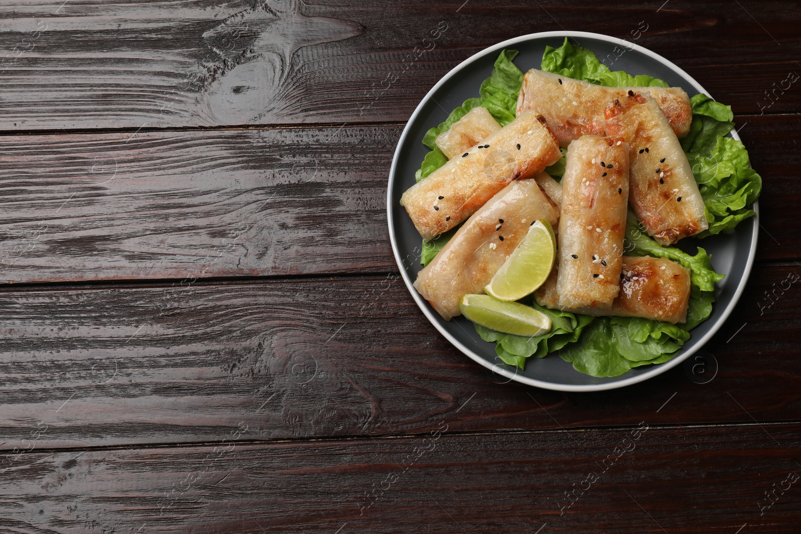 Photo of Tasty fried spring rolls, lettuce and lime on wooden table, top view