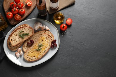 Photo of Tasty bruschettas with oil and rosemary on black table, flat lay. Space for text