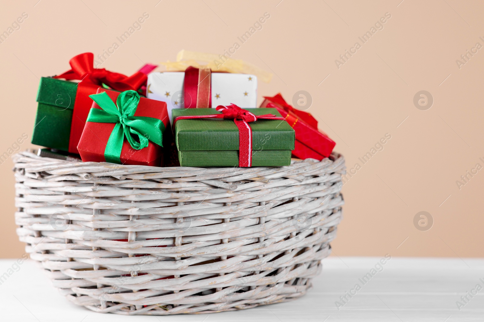 Photo of Wicker basket full of gift boxes on white wooden table against beige background