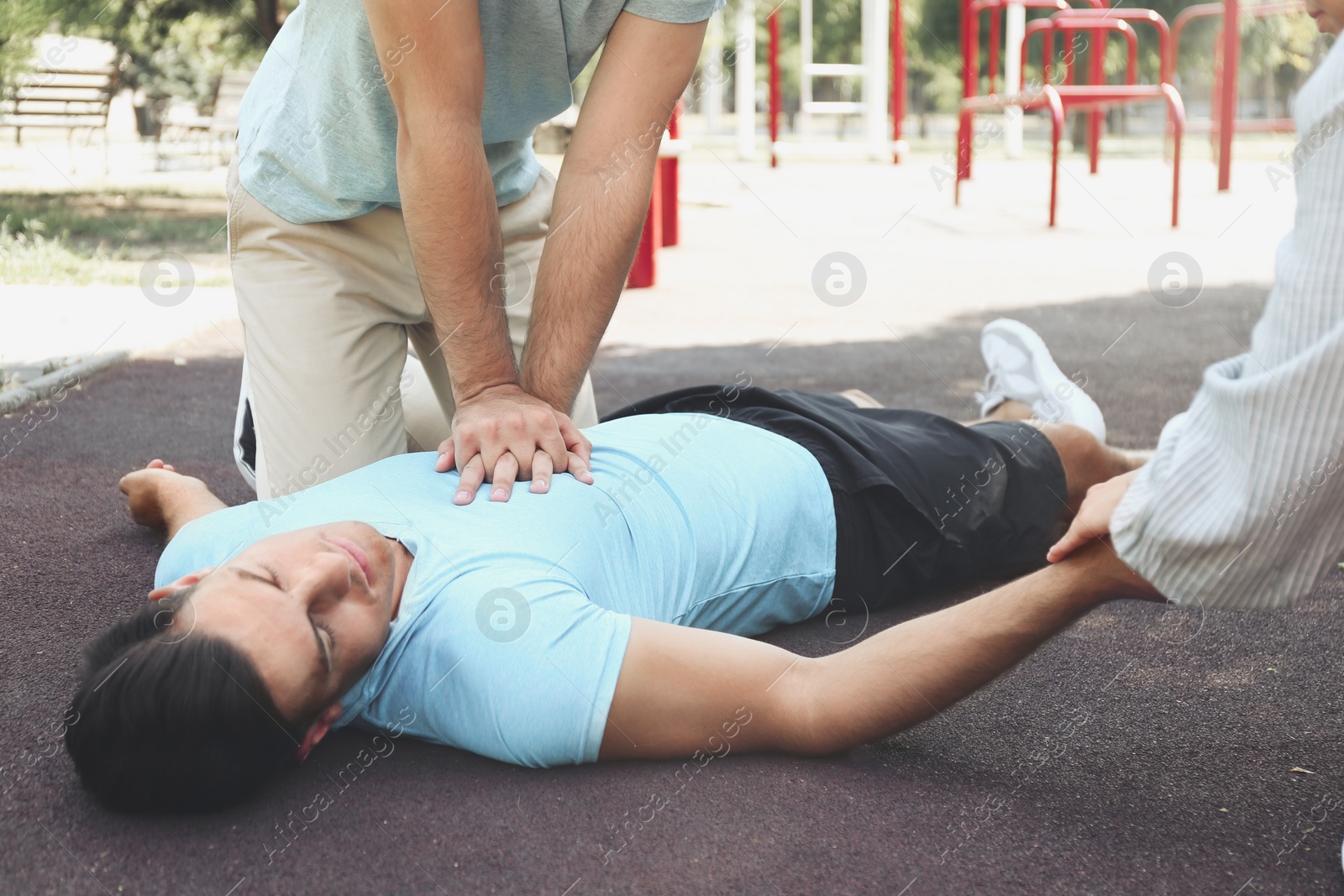 Photo of Passerby performing CPR on unconscious man outdoors. First aid