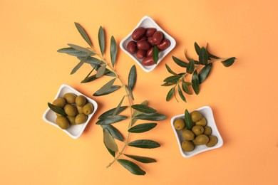 Different fresh olives and green leaves on pale orange background, flat lay