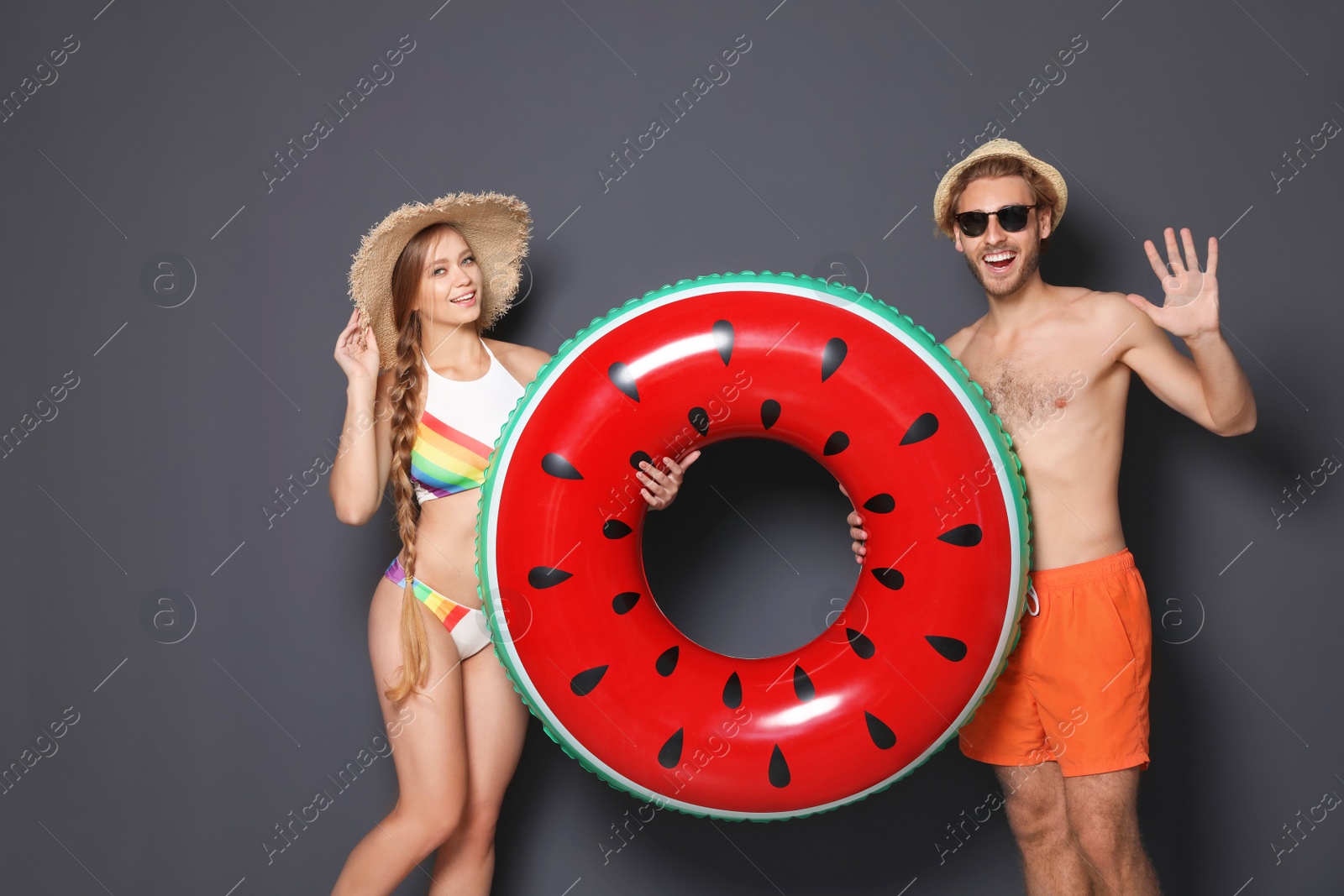 Photo of Young couple in beachwear with inflatable ring on dark background