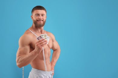Athletic young man with measuring tape and pills on light blue background, space for text. Weight loss