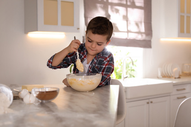 Photo of Cute little boy cooking dough in kitchen at home
