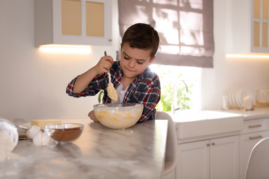 Cute little boy cooking dough in kitchen at home