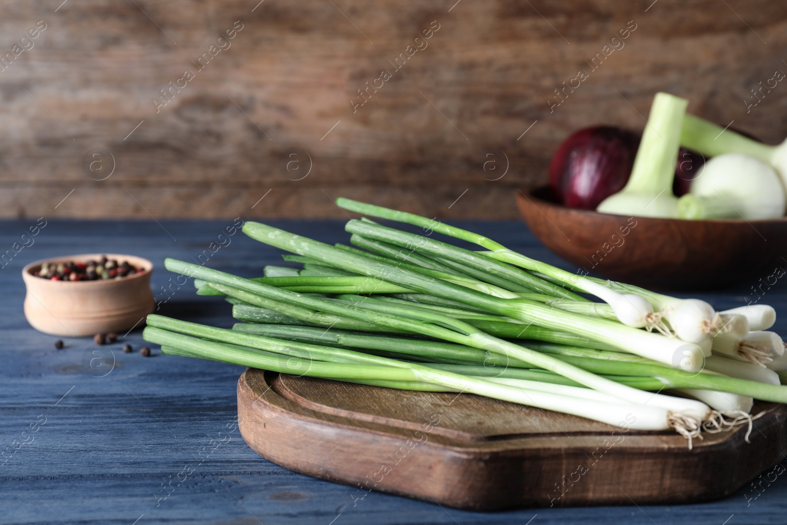 Photo of Wooden board with fresh green onion on blue table