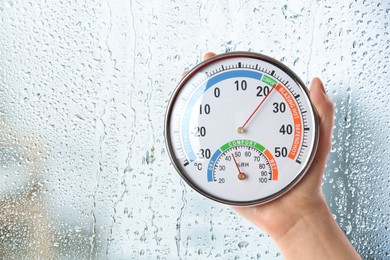 Image of Woman holding hygrometer with thermometer near window on rainy day, closeup. Space for text
