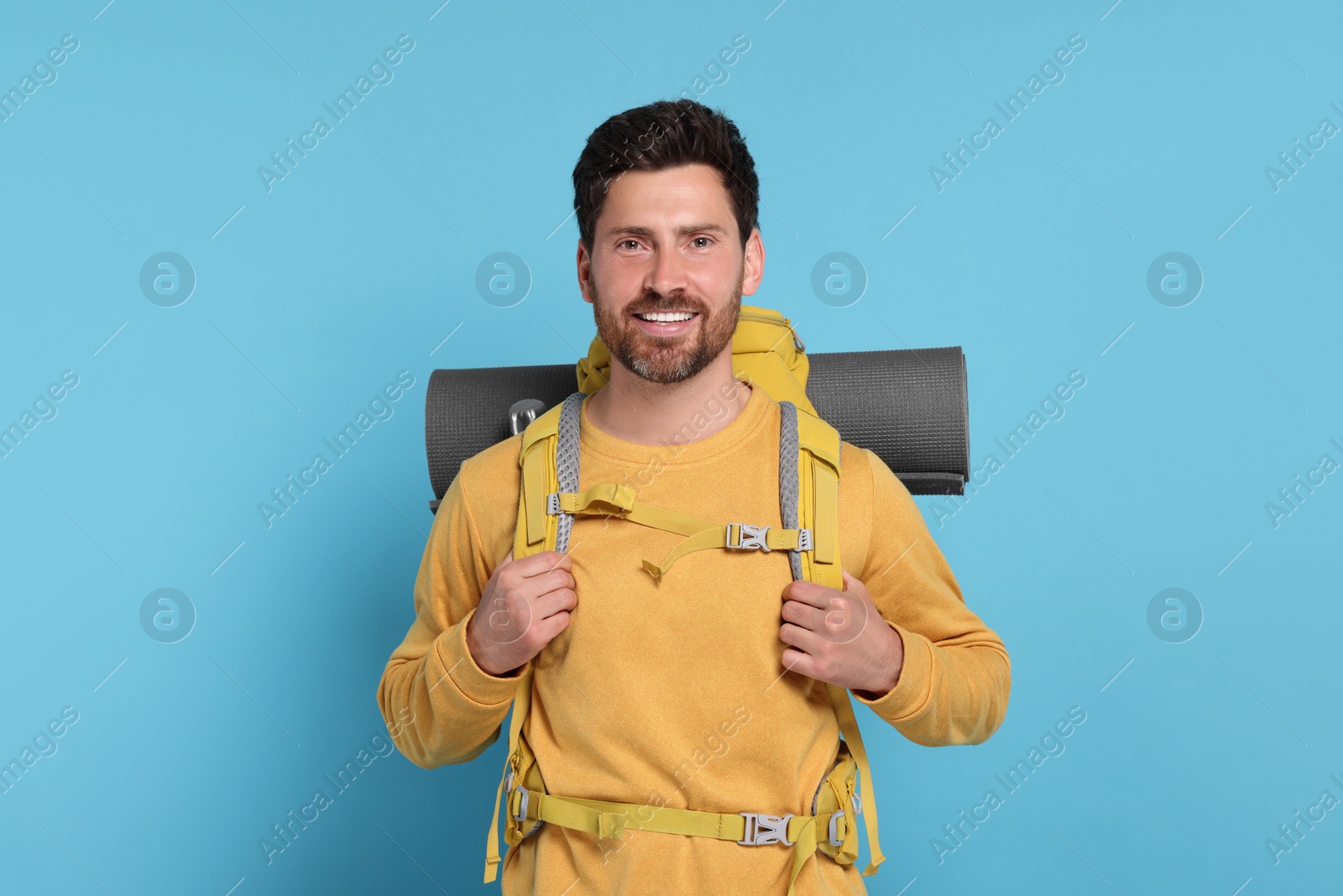 Photo of Happy man with backpack on light blue background. Active tourism