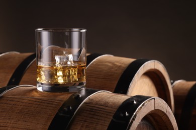 Whiskey with ice cubes in glass on wooden barrel against dark background
