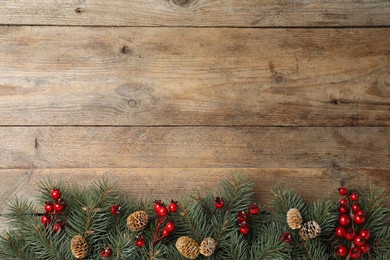 Flat lay composition with fir branches and berries on wooden background, space for text. Winter holidays