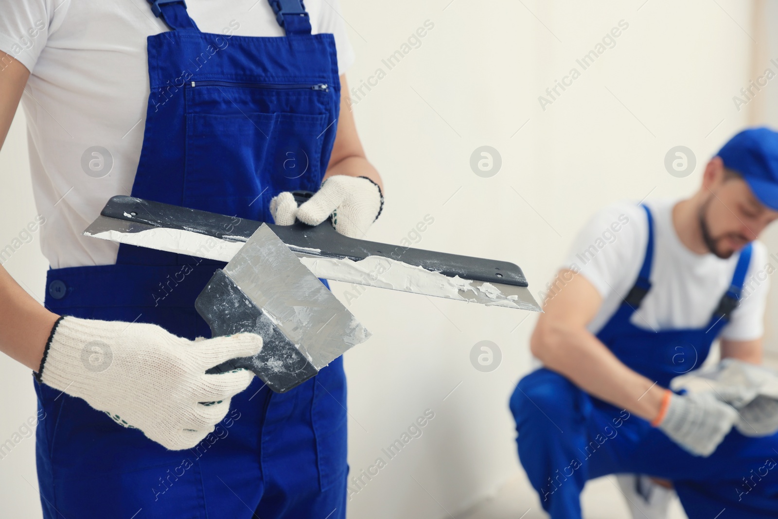 Photo of Professional workers with putty knives near wall indoors, closeup