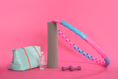 Hula hoop, gym bag, bottle of water, dumbbells and yoga mat on pink background