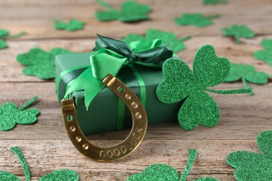 Photo of St. Patrick's day. Golden horseshoe, green gift box and decorative clover leaves on wooden table