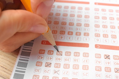 Photo of Woman filling out lottery ticket with pencil on wooden table, closeup. Space for text