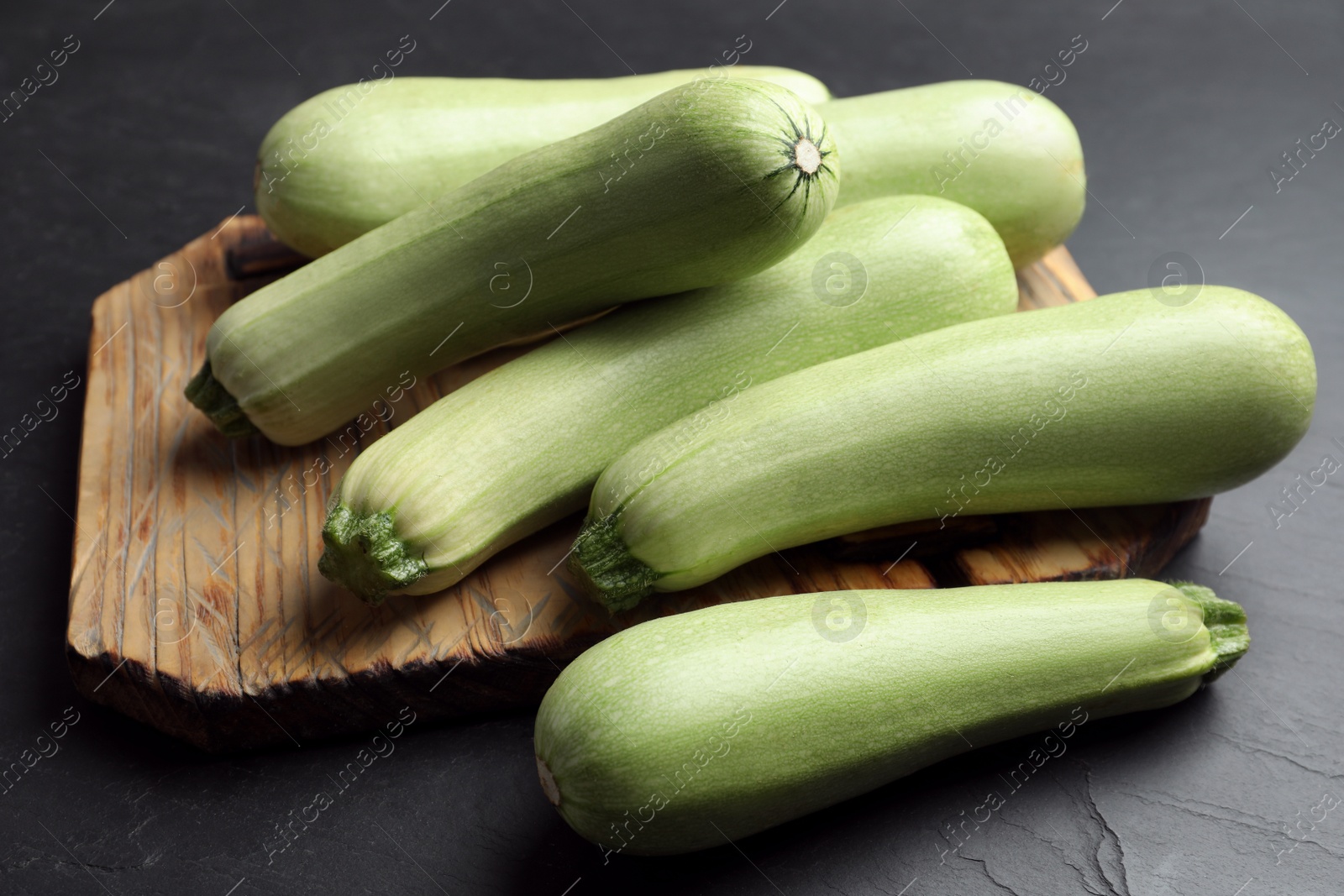 Photo of Raw green zucchinis and wooden board on black slate table