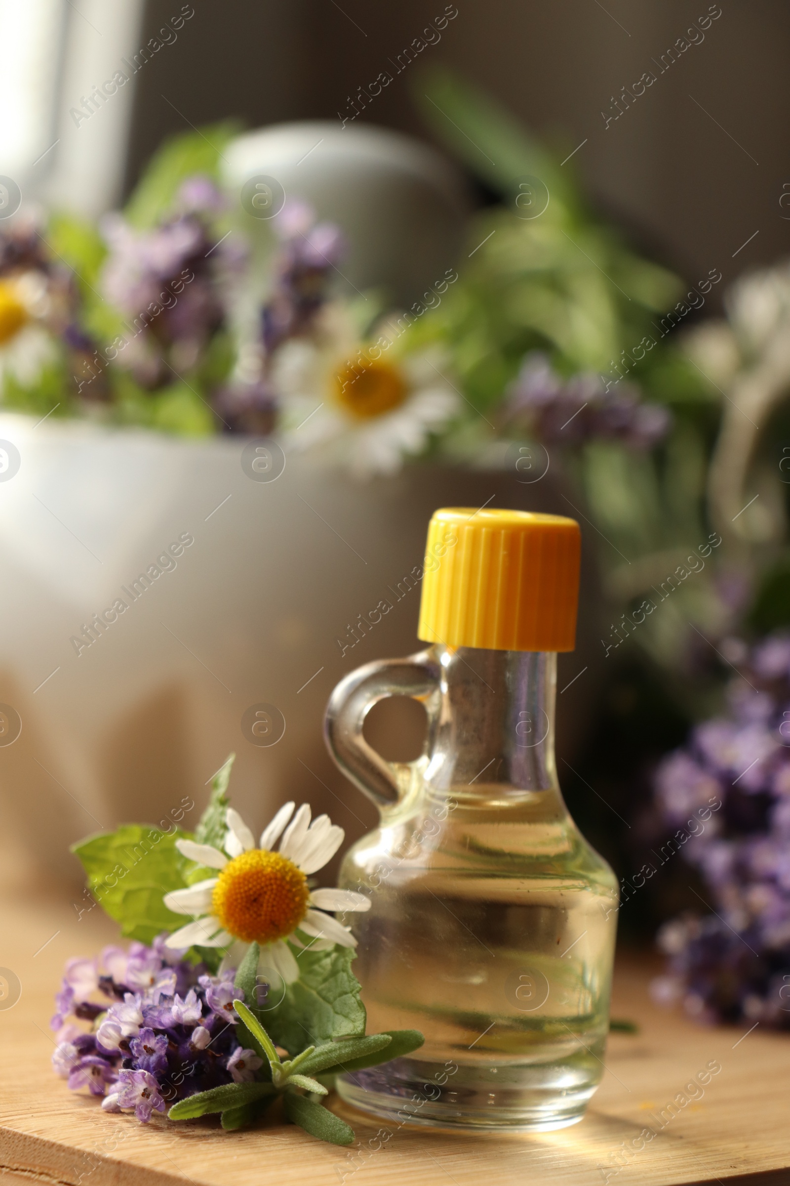 Photo of Bottle of natural lavender essential oil near mortar with flowers on wooden table