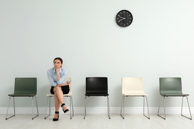Young woman with smartphone waiting for job interview in office hall