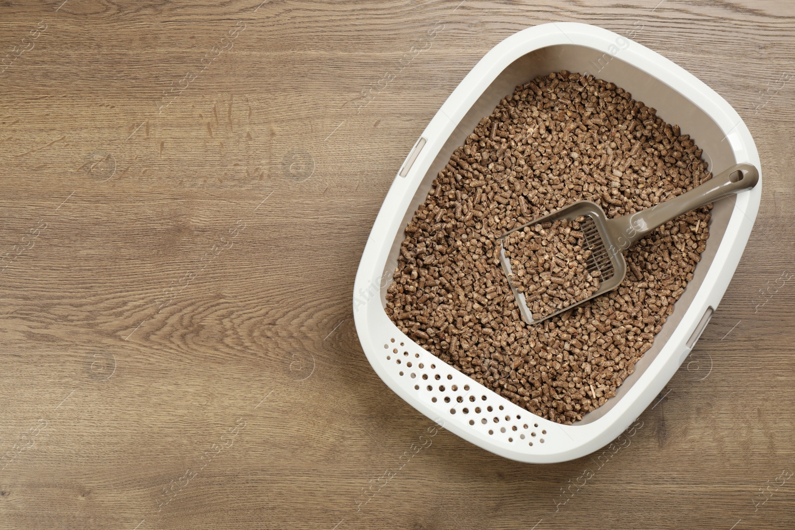 Photo of Cat litter tray with filler and scoop on wooden floor, top view. Space for text