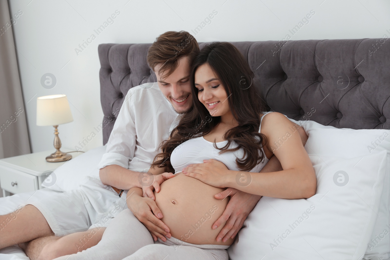 Photo of Young husband and his pregnant wife lying in bed at home