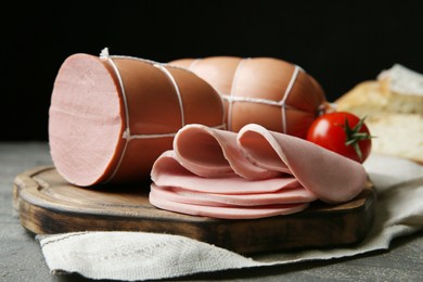 Photo of Board with tasty boiled sausages on dark textured table against black background, closeup