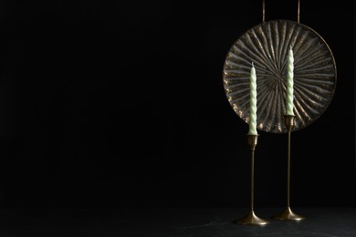 Photo of Vintage metal candlesticks with candles and dish on table against black background, space for text