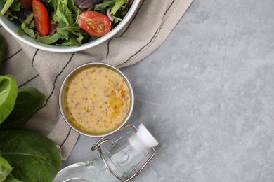 Photo of Tasty vinaigrette in bowl, vinegar and salad on grey table, flat lay. Space for text
