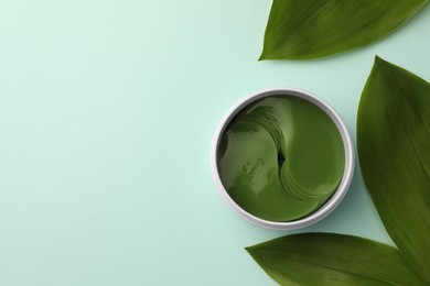 Photo of Jar of under eye patches and green leaves on turquoise background, flat lay with space for text. Cosmetic product