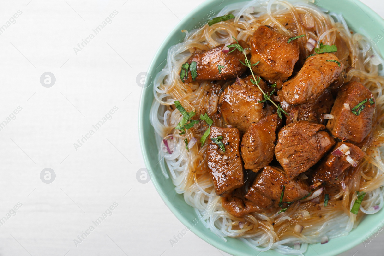 Photo of Bowl with pieces of soy sauce chicken and noodle on white wooden table, top view. Space for text