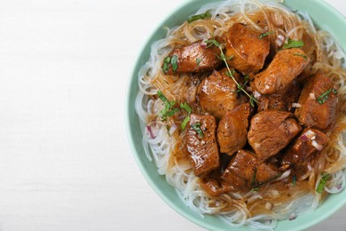 Bowl with pieces of soy sauce chicken and noodle on white wooden table, top view. Space for text