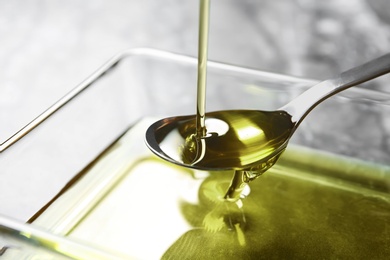 Photo of Pouring hemp oil into spoon over glass bowl, closeup