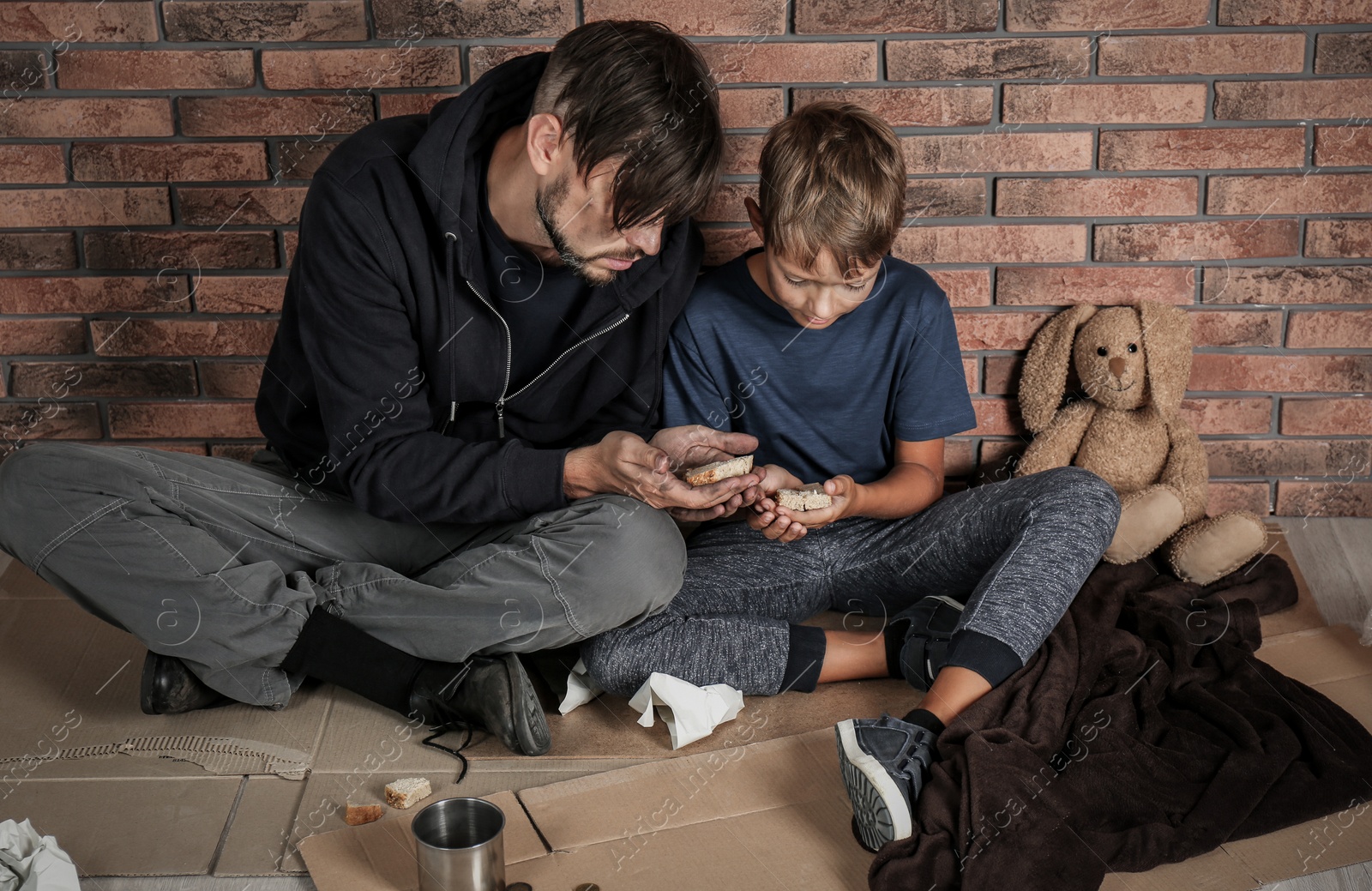 Photo of Poor man and his son sitting om floor near brick wall